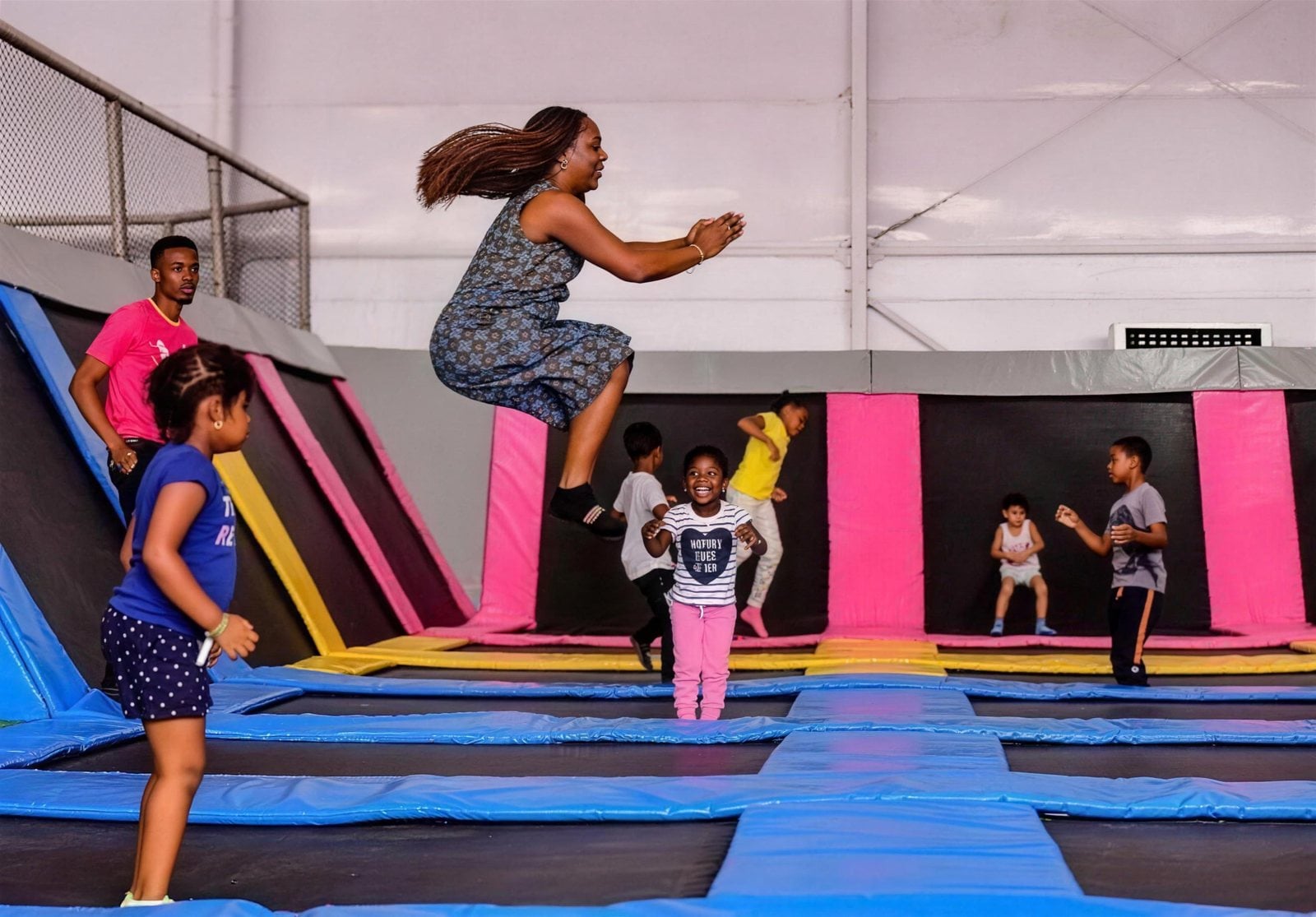 A mum mid-jump at a trampoline park while the kids cheer her on
